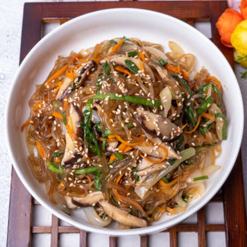 A white bowl of Gohyang Korean Restaurant's japchae, glass noodles with vegetables and sesame seeds.