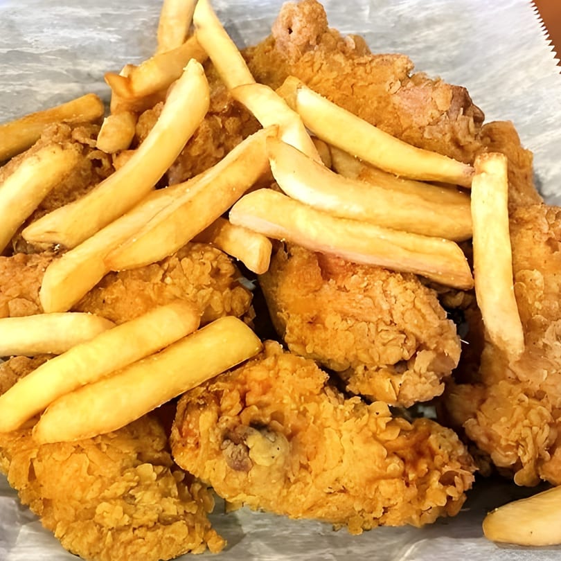Crispy fried chicken pieces and golden french fries served on a white paper liner.