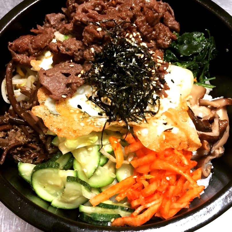 Close-up of a colorful Korean bibimbap bowl with beef, egg, vegetables, and seaweed.
