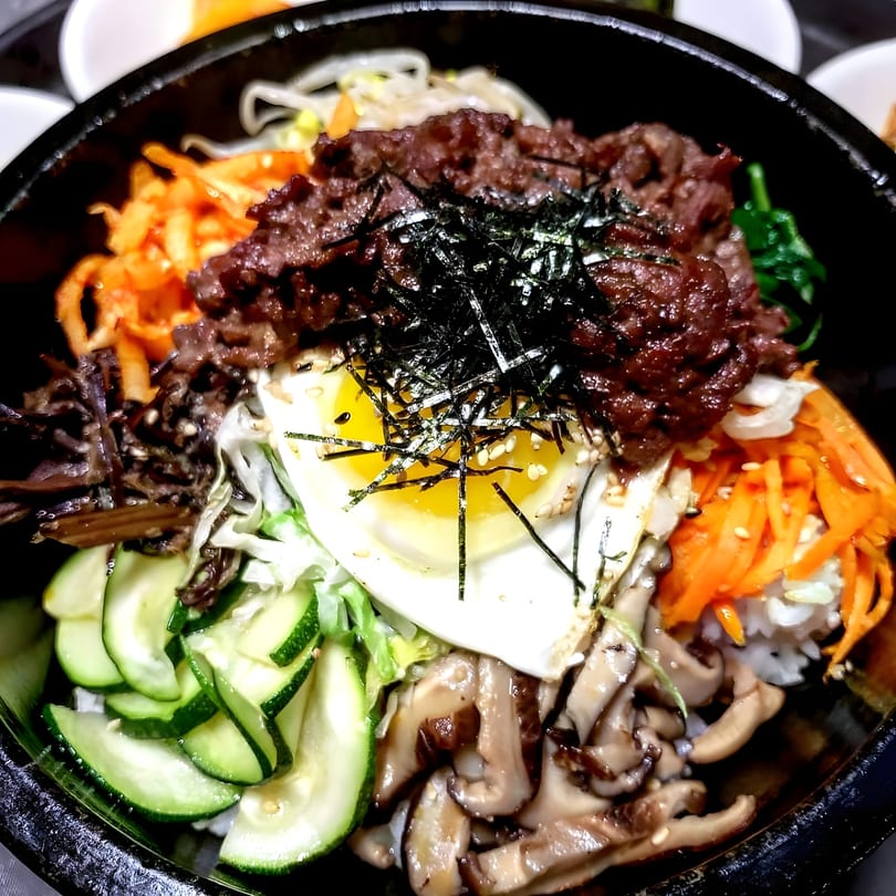 A vibrant Korean bibimbap bowl with beef, egg, various vegetables, and seaweed in a black bowl.