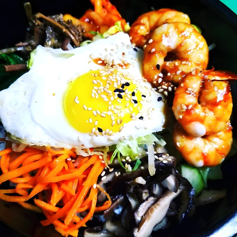 Bibimbap with a fried egg, shrimp, shredded carrots, mushrooms, and sesame seeds.